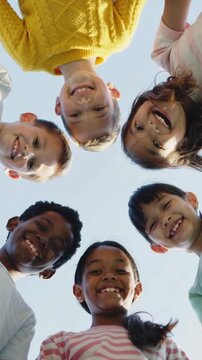 Diverse children looking down into camera lens against bright blue sky background low angle view