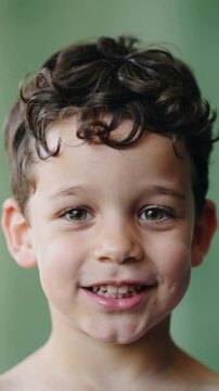 Young boy smiling with curly brown hair against green background close up shot