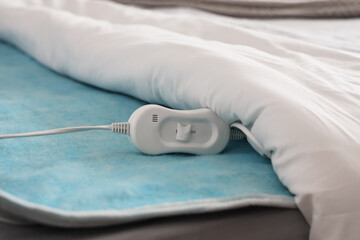 Electric heating pad with controller on bed in room, closeup © Pixel-Shot
