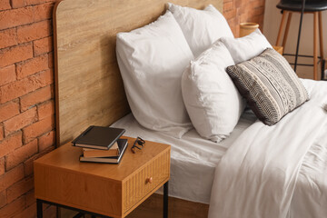 Fototapeta premium Stylish bedside table with books and eyeglasses near cozy bed in bedroom
