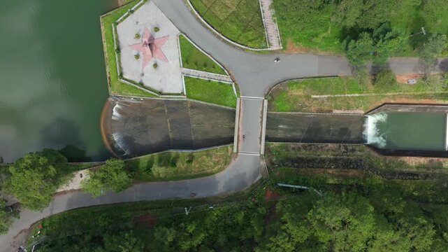 Aerial view of Tuyen Lam Lake dam and reservoir in Da Lat, Vietnam. Water flows over the dam, creating a scenic landscape.