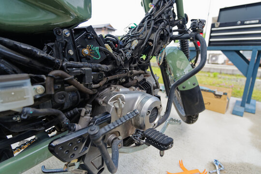 Disassembled motorcycle with exposed engine and wiring during outdoor maintenance and repair work