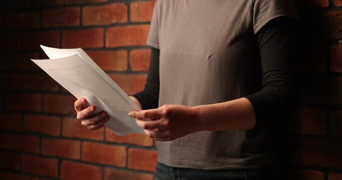 Actor with script rehearsing near brick wall indoors, closeup