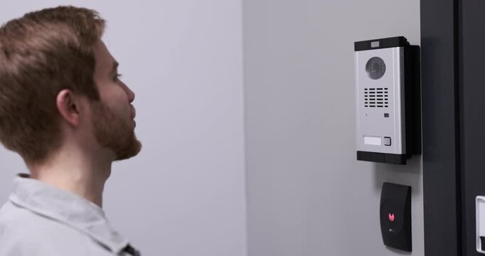 Man pressing button on intercom panel indoors