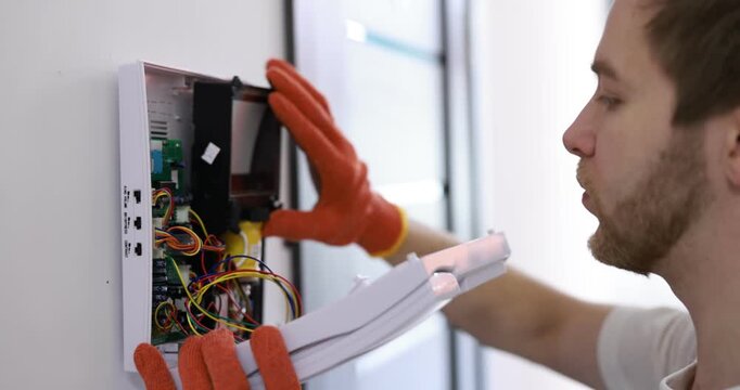 Man with screwdriver installing modern intercom system on wall indoors, closeup. Camera moving in