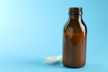 Antibiotic suspension in bottle and spoon on light blue background, closeup. Space for text