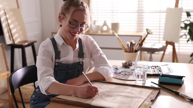 Woman drawing with pencil at table indoors, camera moving in. Slow motion effect