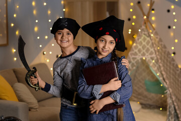 Naklejka premium Cute children dressed as pirates with adventure book at home in evening