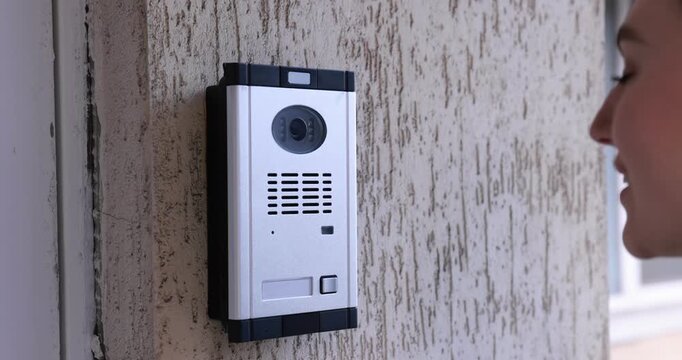 Woman pressing button on intercom panel outdoors, closeup. Camera moving in