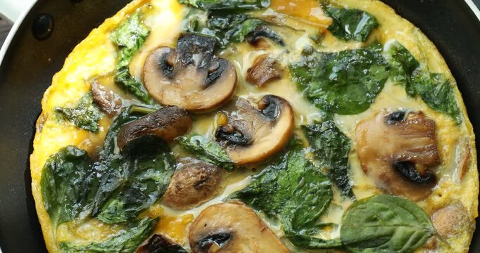 Tasty omelette with spinach and mushrooms on black table, spinning. Closeup view