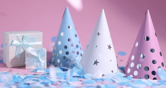 Party hats and gift boxes under falling beautiful confetti on pink background, closeup