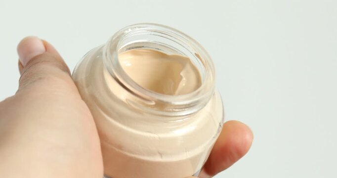 Woman opening jar of skin foundation on white background, closeup