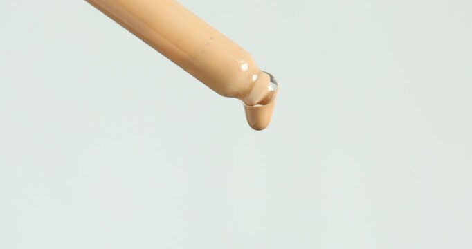 Dripping skin foundation from pipette on white background, closeup