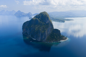 Obraz premium Glassy calm seas bathe the coastline of an idyllic limestone island in El Nido, Philippines. This area in Palawan is a popular vacation destination due to its coral reefs, beaches, and hidden lagoons.