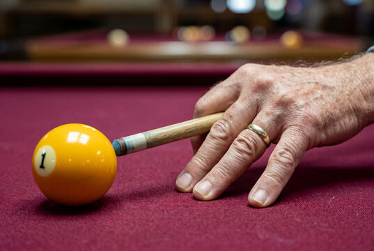 Hand of a senior man holding a wooden cue stick aiming at a yellow billiard ball on a red table