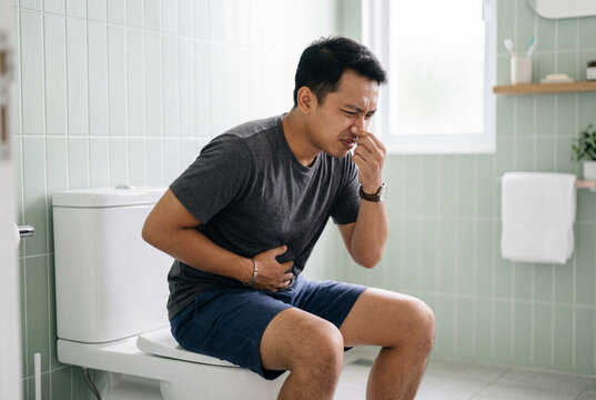 Young adult man experiencing stomach pain while seated on a toilet in a pristine bright bathroom