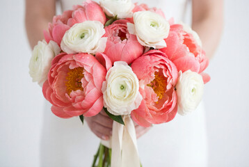 Obraz premium Elegant wedding bouquet of coral peonies and white ranunculus held by bride