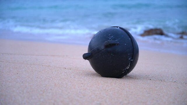 砂浜に打ち上げられた黒いプラスチックの浮きとボケた波打ち際（海洋ゴミ・SDGs）