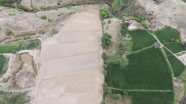Aerial flight revealing the intersection of traditional farming and rural development, featuring cultivated farms, green crops, and modern solar panels next to a homestead