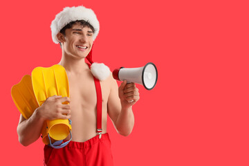 Young man in Santa hat with flippers and megaphone on red background. Christmas in July © Pixel-Shot
