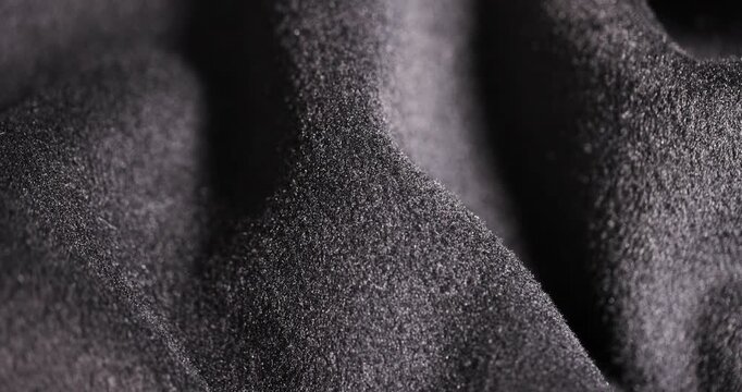 The fleece fabric lies in folds, a dark gray soft fleece with a fleecy texture and deep shadows in side lighting with clear details and an organic surface.