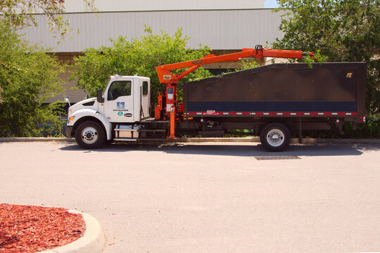 Municipal Landscaping Crane Truck Parked With Debris-Filled Dump Body And Orange Boom At Warehouse. Editorial Use Only St. Petersburg,FL USA May 4, 2026.Bright orange hydraulic boom and white cab sugg