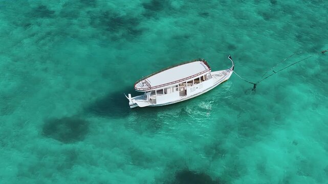 Aerial view of a white traditional boat anchored in the crystal clear turquoise waters above a coral reef in Fulhadhoo, Baa Atoll, Maldives.