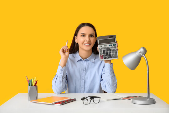 Beautiful young woman with calculator and notebooks at table on yellow background
