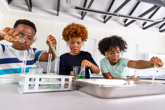 Diverse school-age boys doing chemistry lab at school, wearing safety goggles and using pipettes