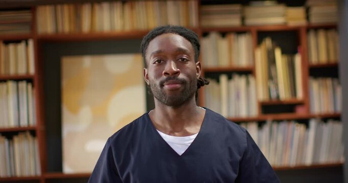 African American man standing by clinic shelf in scrubs reacting to offscreen cue smiling, laughing