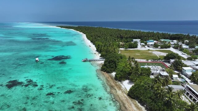 Aerial view of the lush tropical island of Fulhadhoo featuring white sandy beaches, turquoise coral reefs, and dense palm groves in Fulhadhoo, Baa Atoll, Maldives.