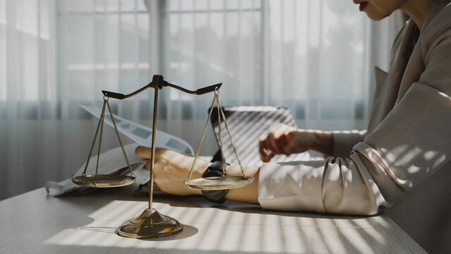 Soft sunlight streams across a polished wooden desk. Woman's hands rest gently near a classic balance scale. Her focused gaze suggests legal or financial deliberation