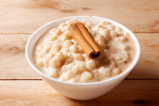 Creamy white corn porridge with cinnamon sticks in a white bowl on a wooden table