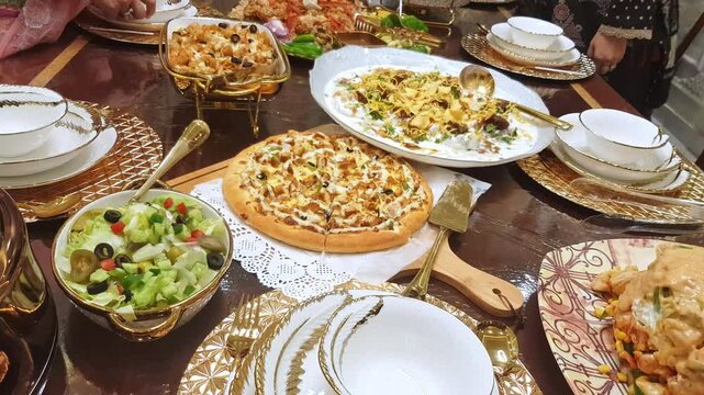 Variety of multiple food dishes, pizza, pasta and vegetable salad includes lettuce, olive and cucumber served in dinner on dining table.