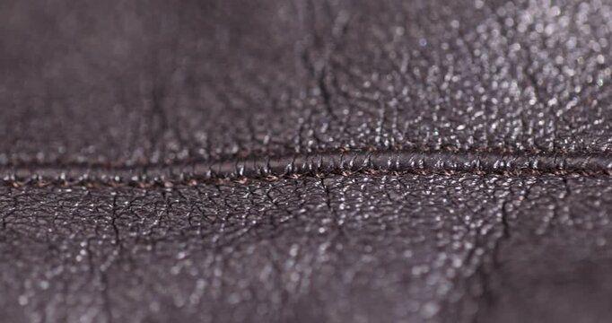 Old black leather with wrinkles, worn leather has a grainy texture and a horizontal connecting seam of threads in the middle of the frame.
