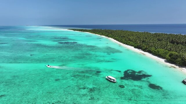 Aerial view of the lush tropical island of Fulhadhoo with white sandy beaches, palm trees, and boats navigating the crystal clear turquoise waters in Fulhadhoo, Baa Atoll, Maldives.