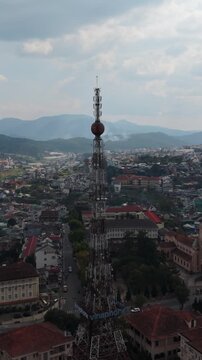 Vertical screen, Vietnam, Da Lat Aerial Dalat Mast Tower Closeup, Engineering Foreground With Lattice Structure, Distant Mountains, Dense City Blocks, Cloudy Sky And Technical Inspection