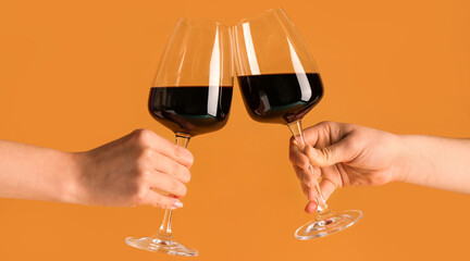 Female hands with glasses of red wine on orange background