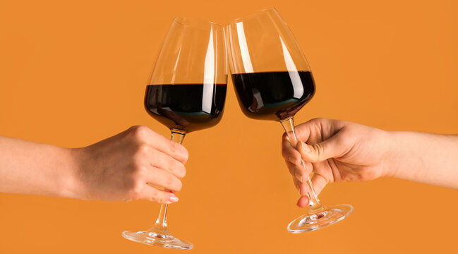Female hands with glasses of red wine on orange background