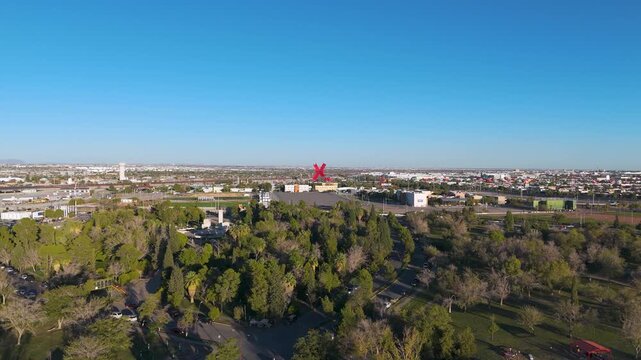 El Chamizal Federal Public Park in Ciudad Juarez, Mexico. The image showcases the expansive green area with numerous trees, walking paths, and recreational spaces. In the background, the iconic red X.