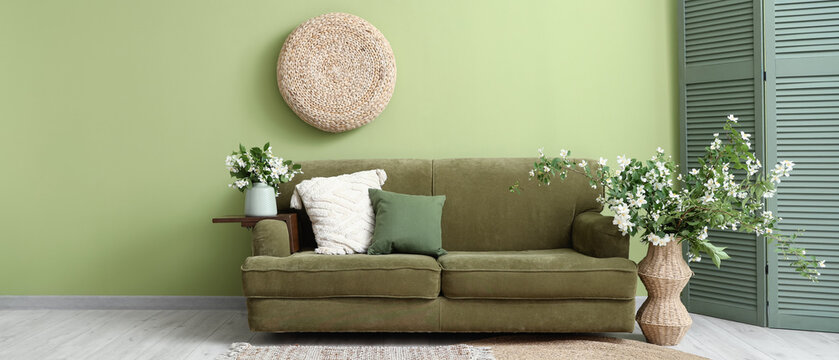 Interior of living room with sofa, folding screen and vases with blooming jasmine flowers