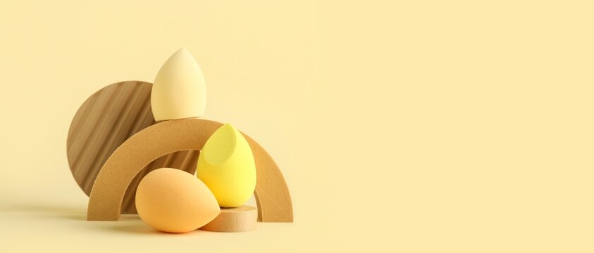 Decorative podiums and makeup sponges on yellow background with space for text