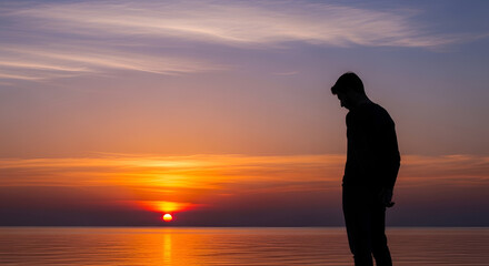 Fototapeta premium Silhouette of a man looking down at the ocean during a vibrant sunset over the water