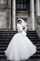 Obraz premium Beautiful bride standing on historic staircase in elegant wedding dress with dramatic romantic atmosphere and timeless European architecture. Charming bridal lifestyle portrait ideal for wedding