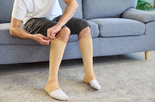Man wearing compression socks for varicose veins. Beige hosiery supports legs at home, improving circulation and easing swelling and pain. Concept medical compression therapy for thrombosis.