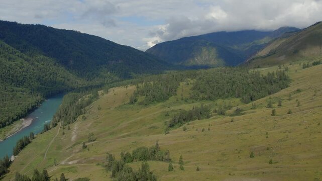 Drone footage of Ak-Kem valley with a winding turquoise river, forested slopes and open meadows under cloudy sky in the Altai Republic, Russia
