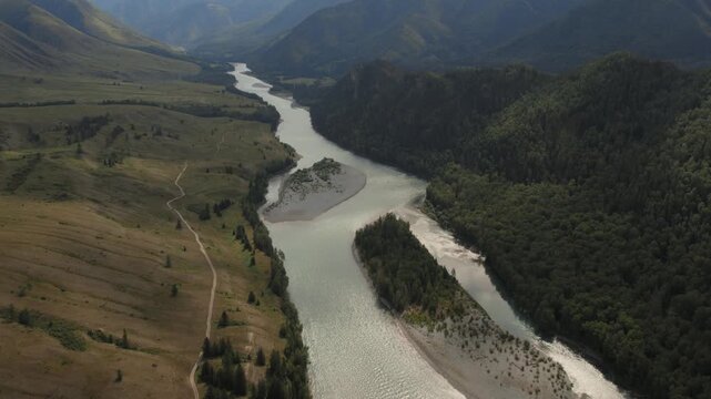 Drone footage of a winding river with sandbars and forested slopes in Ak-Kem Valley, Altai Republic, Russia, surrounded by rolling hills and mountains
