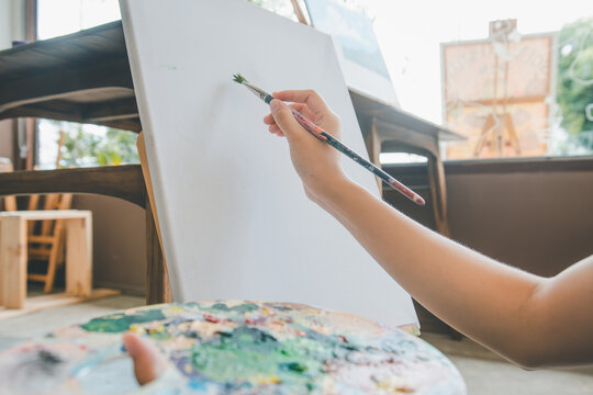 close-up art student's hand using watercolor paint brush painting on canvas doing some art projects on studio workshop