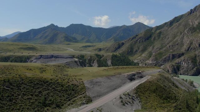Drone footage of the confluence of the Chuya and Katun rivers near Inya, Altai Republic, Russia, with mountain valley, cliffs and winding road on a sunny day