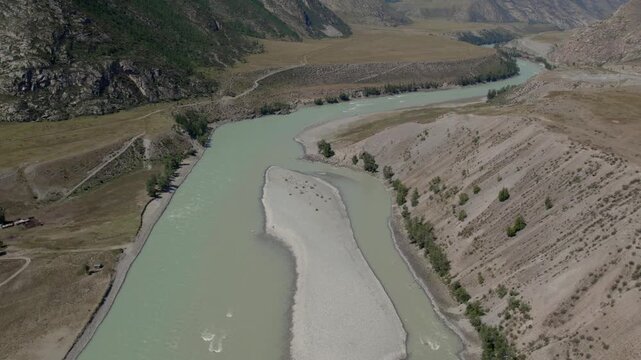 Drone footage of the turquoise Katun River meeting the silty Chuya River in a wide mountain valley near Inya, Altai Republic, Russia, on a sunny day